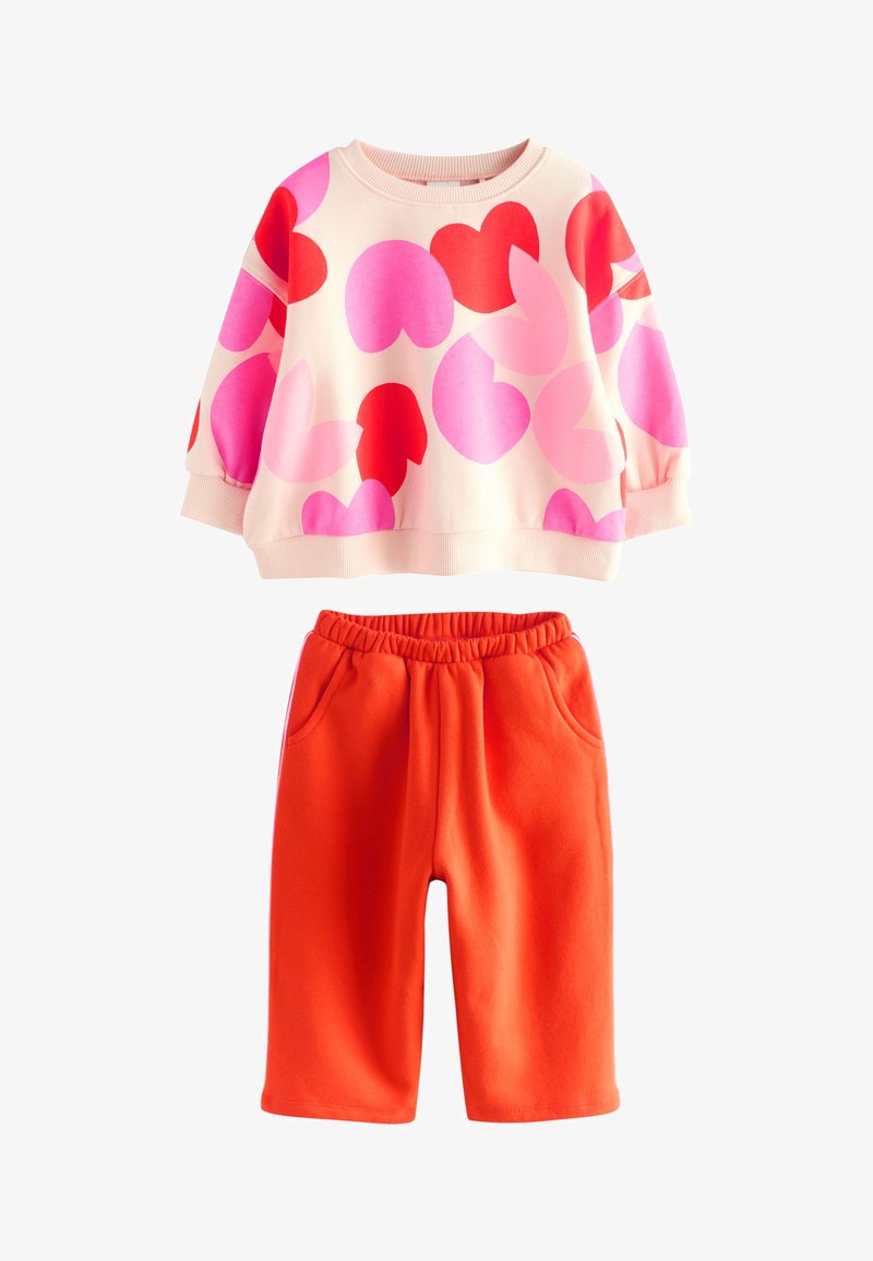 Tenue pour enfants avec un sweat-shirt crème orné de formes de cœurs roses et rouges, et un pantalon à taille élastique orange vif avec poches.