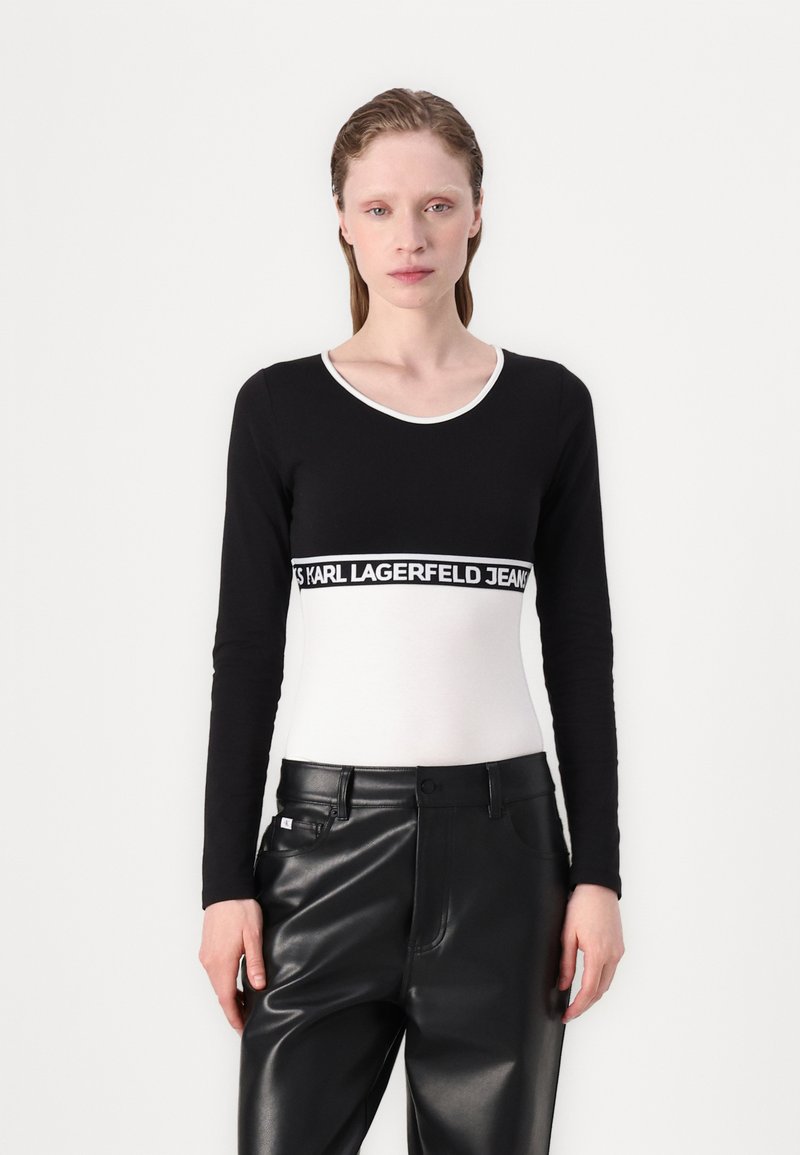 Black long-sleeve top with white accents and a branded waistband, paired with high-waisted black faux leather pants. Smooth texture.