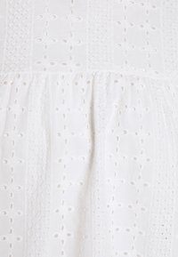 Tissu blanc avec des motifs brodés et des découpes, mettant en valeur un design texturé et superposé avec une apparence douce et légère.