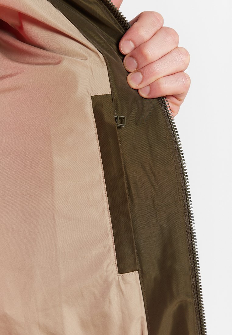 Futter der Reißverschlussjacke mit kontrastierender Farbpalette: zartrosa Futter mit einer strukturierten olivgrünen Außenschicht und einem kleinen Taschendetail.