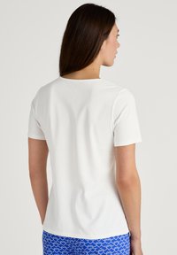 Witte t-shirt met korte mouwen en een ronde halslijn, gemaakt van zachte stof. De achterkant is glad en onversierd, gecombineerd met blauwe met patroon bedrukte broek.