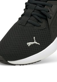 Chaussure de sport noire avec une tige en mesh, semelle blanche et accent logo gris. Des motifs texturés sur le côté ajoutent des détails au design.