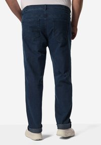 Dunkelblaue Jeans mit geradem Schnitt, ausgestattet mit zwei Gesäßtaschen und einem umgeschlagenen Saum, getragen mit hellen Sneakers.