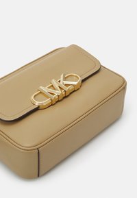 Tan leren handtas met een rechthoekige vorm, een klepsluiting en een opvallend goudkleurig logo-accessoire aan de voorkant. Gladde textuur.