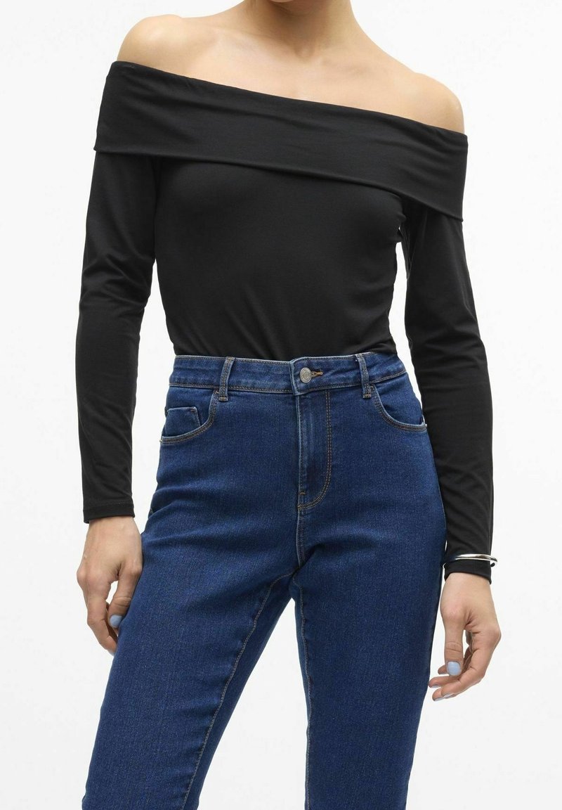 Musta olkaimeton pitkähihaisuus toppi yhdistettynä korkeavyötäröisiin sinisiin farkkuihin, joissa on istuva muotoilu ja klassinen viiden yrityksen tyyli.