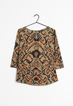 Haut beige à manches longues avec un motif abstrait noir et orange, présenté sur un cintre noir sur fond blanc.