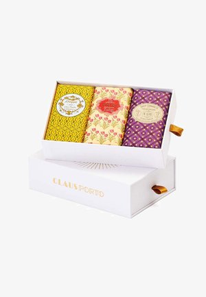 Three decorative soap bars in a white box. Yellow, floral, and purple patterned wrappings with labels. Box features a gold logo and ribbon.
