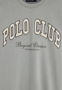 Grå sweatshirt med "POLO CLUB" i store blokbogstaver, "Beyond Classics" i kursiv og "ESTABLISHED 2012" nedenunder.
