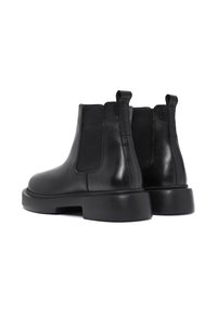 Botas de tobillo de cuero negras con paneles elásticos, punteras redondeadas y suelas de goma gruesas, con bucles en la parte trasera. Textura suave.