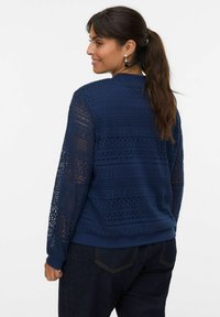 Granatowy sweter z wyszukanym wzorem koronkowym, z długimi rękawami i ściągaczami. Lekka struktura z wzorzystymi detalami.