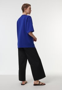 Camiseta azul de corte holgado con hombros caídos, combinada con pantalones anchos negros y sandalias planas negras. Textura simple y suave en todo el conjunto.