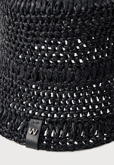 Chapeau seau en paille noire tissée avec un motif à tissage ouvert et une petite étiquette en cuir noir avec un "W" argenté sur le bord.