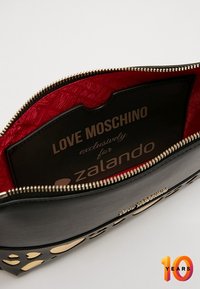 Černá syntetická kožená taštička se zlatými výřezy a červeným podšívkou, uvnitř s logovou kartou Love Moschino x Zalando.