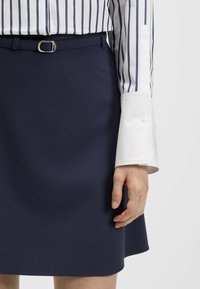 Granatowa spódnica w kształcie litery A z gładkiego materiału, z paskiem w talii i srebrną pętelką na pasek. Biała koszula w niebieskie pionowe paski z zapięciem na guziki przy mankietach.