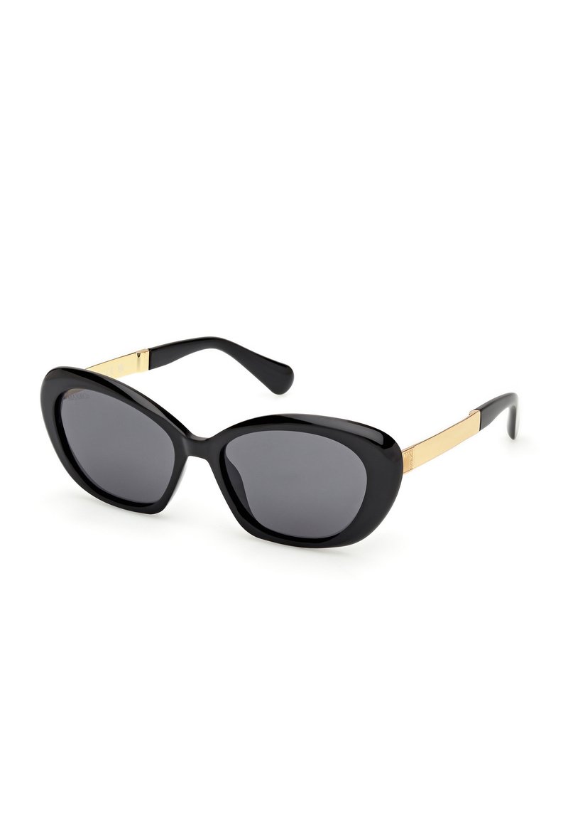 Gafas de sol negras con forma de ojo de gato redondeada, con lentes oscuros y acentos de metal dorado en las patillas. Montura de plástico brillante.