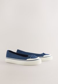 Paire de chaussures en toile bleu marine à enfiler avec semelles en caoutchouc blanches et bouts renforcés à l'avant, présentée sur un fond clair.