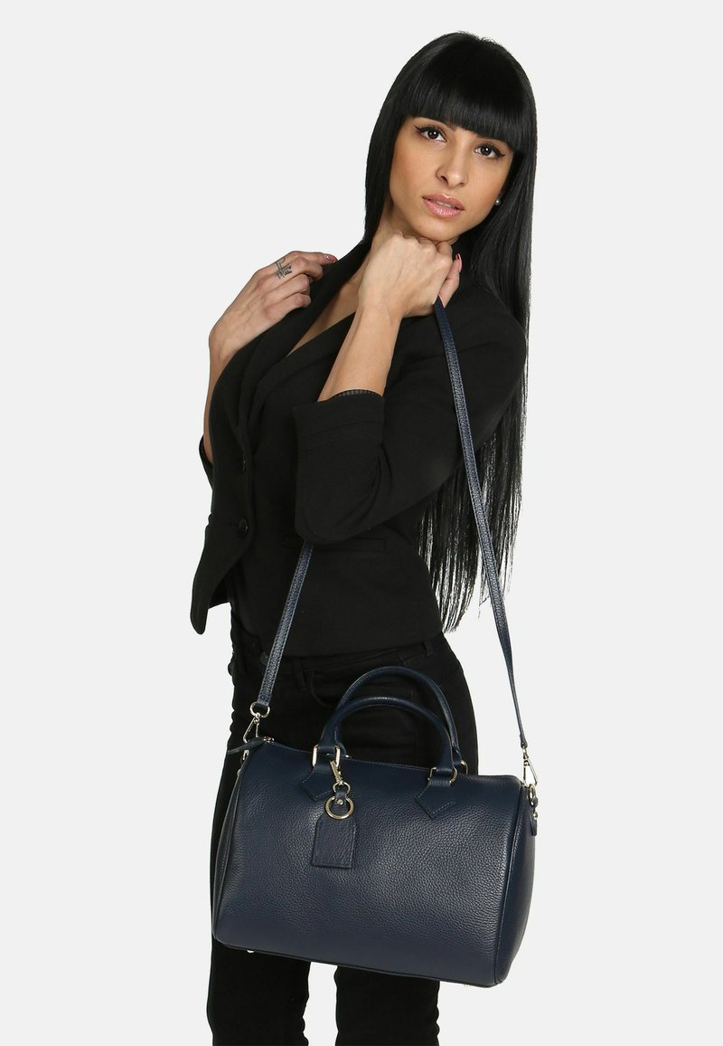 Tmavě modrá kožená kabelka s texturovaným povrchem, kulatým tvarem, dvojitými uchy a odnímatelným ramenním popruhem. Obsahuje stříbrné kovové detaily.