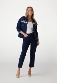 Tamsios džinsinio audinio striukė su raštuotais pečiais, balta palaidinė, tamsūs aukštu liemeniu džinsai ir nuogos aukštakulnės bateliai. Lygus tekstūros paviršius ir prigludusi išvaizda.