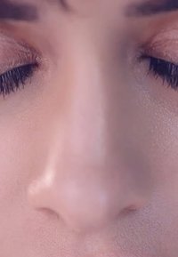 Närbild av ett slätt, ljust ansikte med slutna ögon, en subtil näsa och texturerad hud med mjuka höjdpunkter. Inga synliga sminkprodukter.