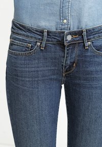 Vaqueros de denim azul oscuro con un ajuste clásico, que cuentan con cinco bolsillos, costuras sutiles y un cierre de botón en la cintura.