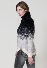 Črna do siva ombre turtleneck pulover iz teksturiranega pletenja, z rebrastim robom in kontrastnimi kremnimi detajli. Nošeno z sivim džinsom.