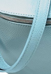 Hellblaues, strukturiertes Lederetui mit einem Reißverschluss und einem dünnen Riemen. Hat sichtbare Nähte und eine abgerundete Form.