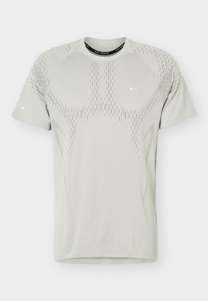 T-shirt de sport gris clair à manches courtes avec motif perforé et petits logos Nike swoosh blancs sur la poitrine et la manche.