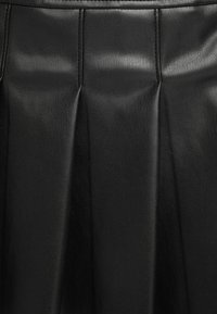 Schwarzer Lederrock mit Falten, strukturierter Oberfläche und glattem Finish. Das Design beinhaltet dezente Linien und eine taillierte Passform.