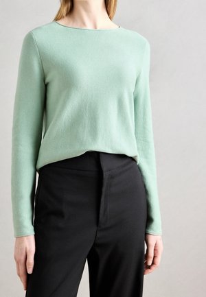 Vaaleanvihreä neulepaita, jossa on pyöreä pääntie, pitkät hihat ja rento istuvuus, yhdistettynä mustiin housuihin, joissa on sileä pinta.