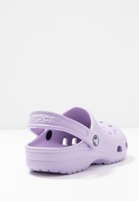 Clogs Crocs de culoare violet deschis cu vârf rotund, orificii de ventilație și curea pe spate. Fabricate dintr-un material ușor, cu o talpă texturată.