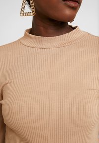 Maglione a collo alto a costine beige con un design aderente e un collo alto. Presenta una texture liscia e un intricato motivo a costine.