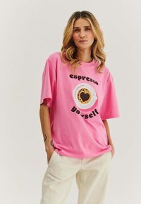 Růžové bavlněné tričko s kulatým grafickým motivem šálku kávy se srdíčkem a textem "espresso yourself" v černé barvě. Oversized střih.