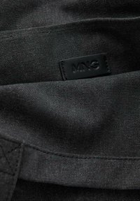 Interior din material textil negru, cu un etichetă din piele embosată cu "MNG". Suprafață texturată, cusături curate și un design simplu, fără ornamente.