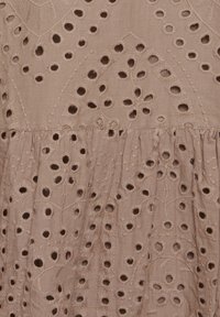 Vyšívaná látka v měkké béžové barvě s vyřezávanými květinovými vzory. Obsahuje texturované prošívání a nařasený lem.