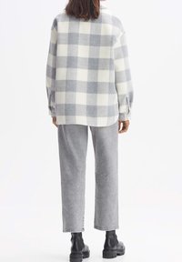 Camisa de forro polar en cuadros blancos y grises con un ajuste relajado, combinada con pantalones anchos grises y botas negras gruesas.