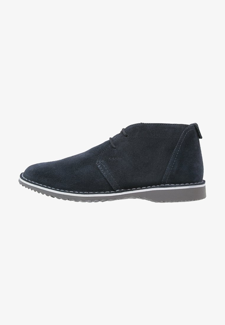 Bottine en daim noir pour homme avec deux œillets pour lacets, semelle cousue blanche et semelle extérieure en caoutchouc gris, vue de profil latéral.