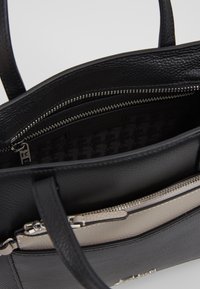 Černá kožená kabelka s texturovaným povrchem, stříbrnými detaily, dvojitými oddíly a geometricky vzorovanou podšívkou.