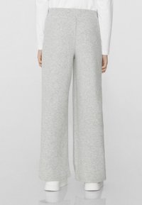 Šedé kalhoty s širokými nohavicemi vyrobené z měkkého fleecového materiálu. Mají elastický pas a hladkou texturu. Nosené s bílými teniskami.