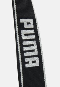 Bandoulière en tissu tissé noir et blanc avec le nom de la marque "PUMA" brodé en lettres blanches épaisses.
