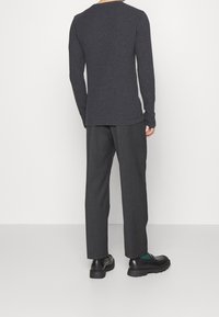 Un haut à manches longues gris foncé avec un col rond, associé à un pantalon large gris foncé et des chaussures noires. Tissu lisse sans motifs.