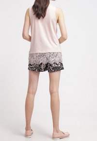 Top senza maniche di un rosa chiaro abbinato a pantaloni corti neri con sovrapposizione in pizzo floreale. I pantaloni corti presentano un tessuto liscio e decorato con una vestibilità comoda.