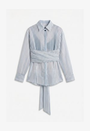 Chemise blanche à manches longues avec des rayures verticales noires, une large ceinture assortie nouée à la taille, et un col avec fermeture à boutons.