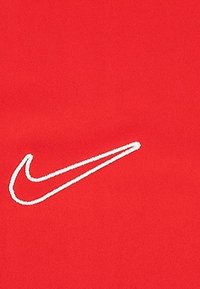 Czerwony materiał z białym haftowanym logo Swoosh Nike, gładka tekstura i minimalistyczny design.