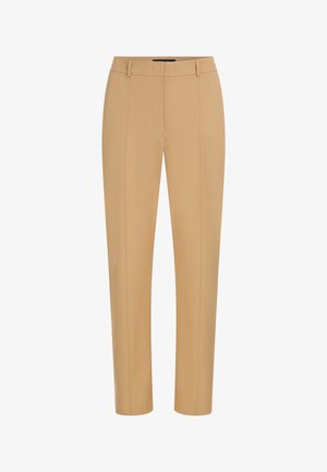 Pantalon beige ajusté sur mesure avec coutures frontales, passants de ceinture et fermeture frontale dissimulée.