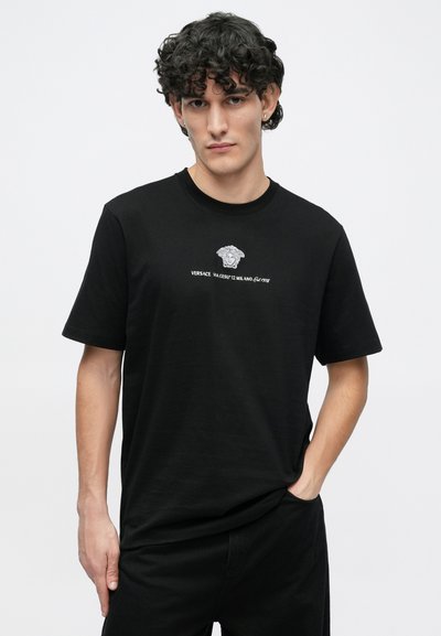 Μαύρο βαμβακερό t-shirt με κεντρικό γκρίζο λογότυπο Medusa και κείμενο "VERSACE VIA GESU' 12 MILANO Est. 1978" σε λευκό. Μανίκια κοντά.