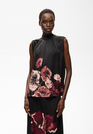 Femme portant un haut noir sans manches et une jupe avec de grands motifs floraux roses et bordeaux sur la moitié inférieure de chaque vêtement.