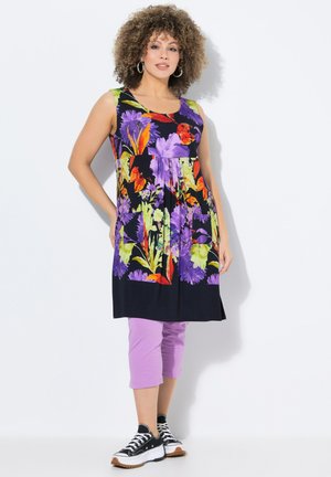 Tunika floreale con una base nera, caratterizzata da fiori vivaci di colore viola, arancio e verde. Abbinata a pantaloni capri lavanda e sneakers nere.