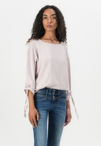 Lys rosa stripete topp med firkantet utringning og samlet ermer, kombinert med blå denimjeans med knappeåpning og slitte detaljer.