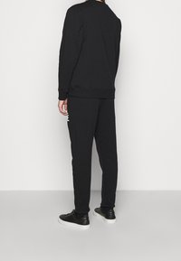 Conjunto de sudadera y pantalones deportivos negros, con un corte relajado y puños acanalados. Zapatillas negras con suelas blancas completan el atuendo.