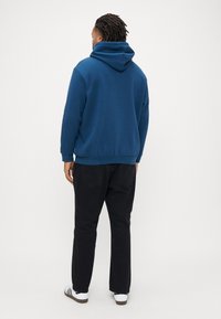 Hanorac albastru cu glugă, croială lejeră, manșete și tiv tricotate, material texturat, asortat cu pantaloni negri și adidași albi.